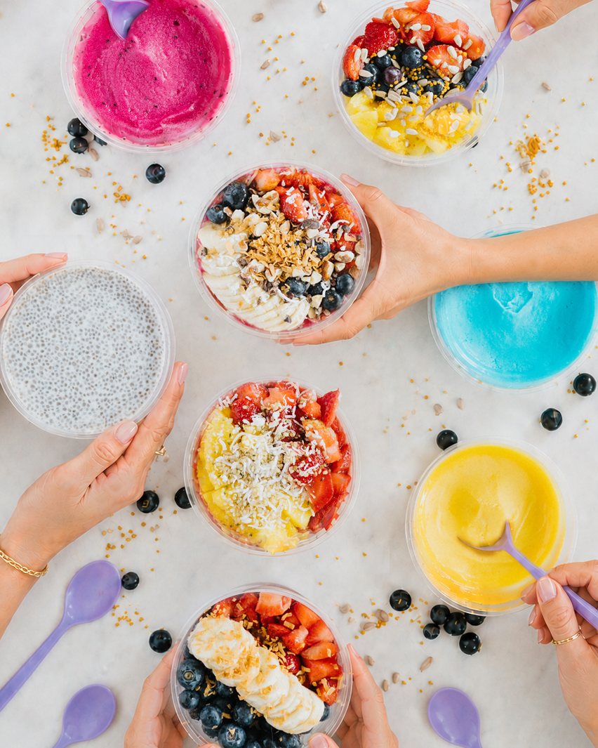 Hands sharing a colorful catering spread of Earth Bowl superfood bowls