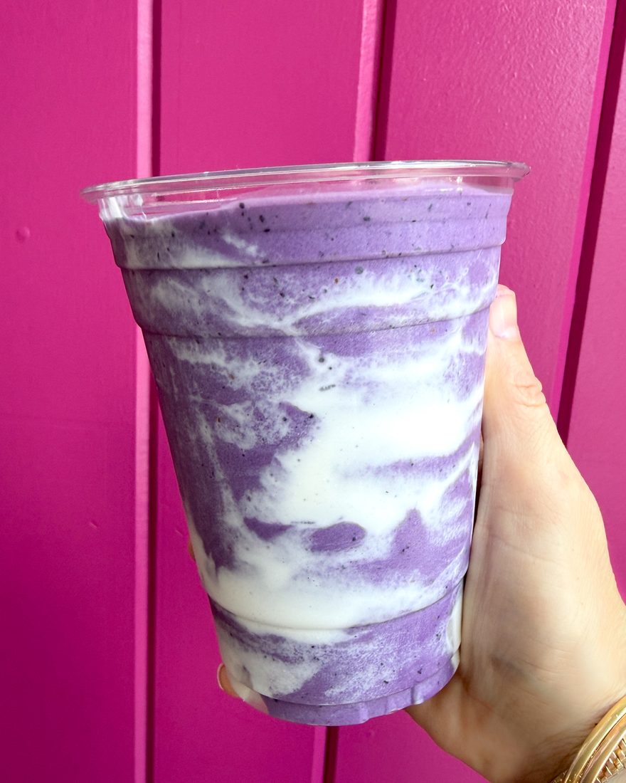 An ube whip shake swirled purple and white against a pink wall