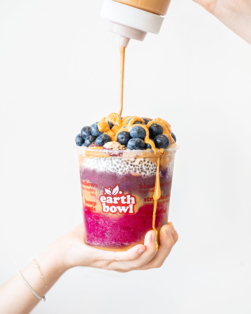 Peanut butter being drizzled over a layered Earth Bowl cup